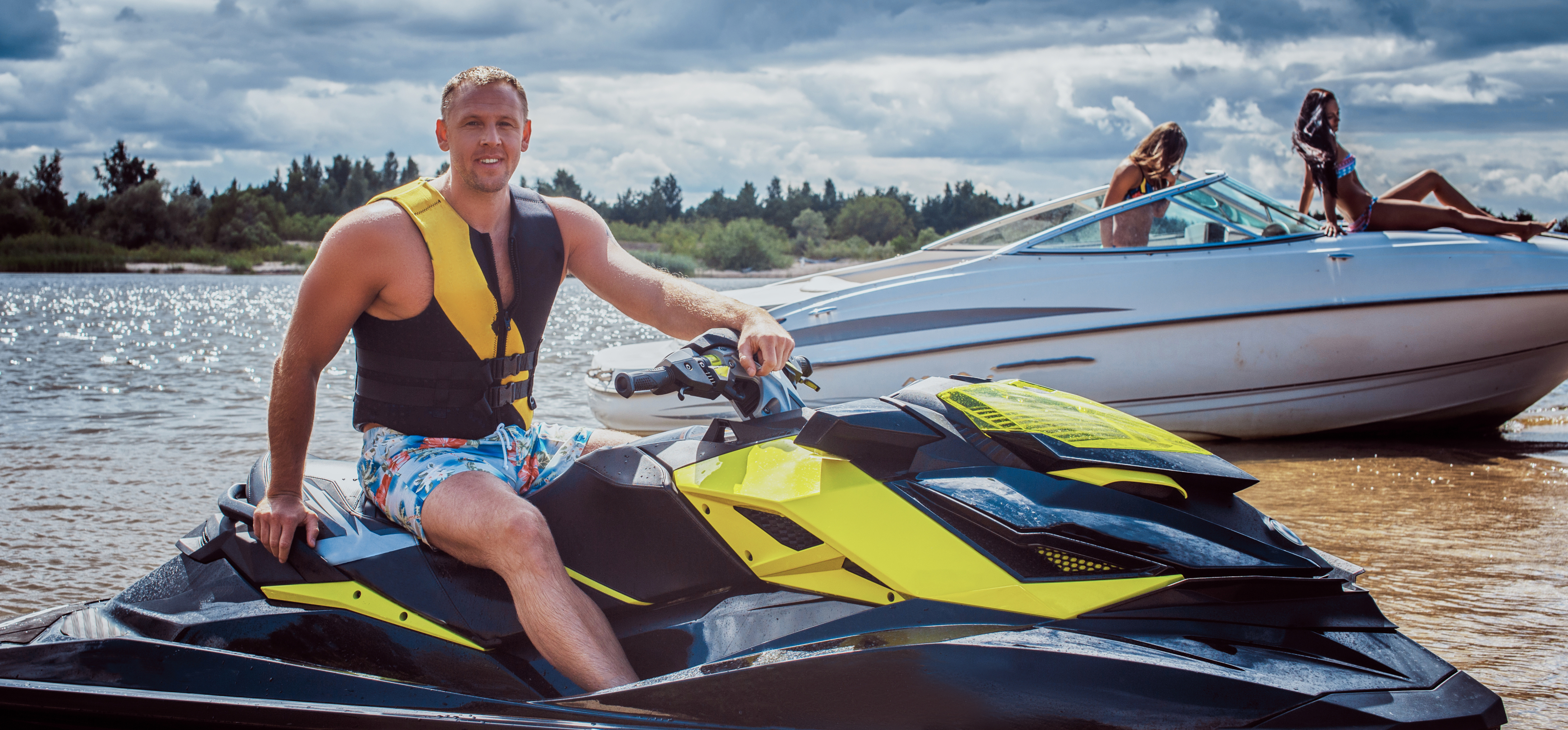 A man is sitting on a jet ski. Two women are on a boat.